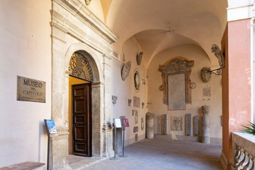 An entrance to Museo del Capitolo with classical architecture, including an arched doorway and stone columns. 1