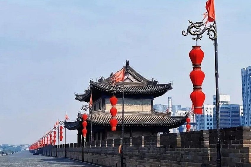A traditional Chinese building with red lanterns and a tiled roof, situated by a body of water with modern buildings in the background. 5