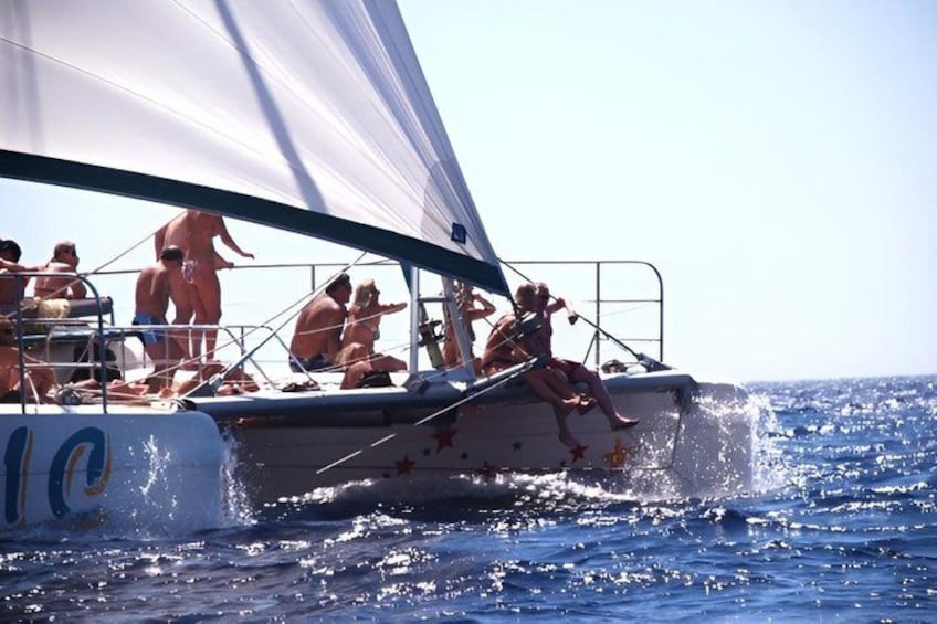 A sailboat with people on deck, water splashing around, and a clear blue sky. 5