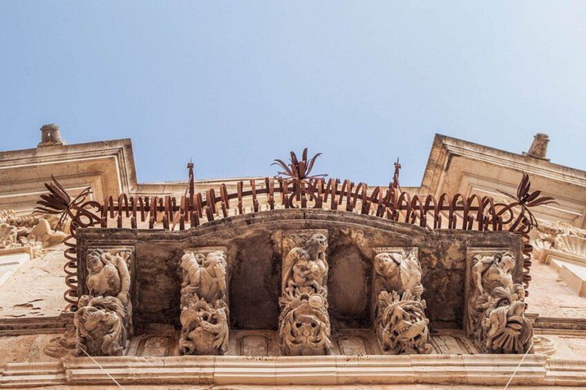 A detailed stone facade with ornate carvings and a decorative metal railing. 4