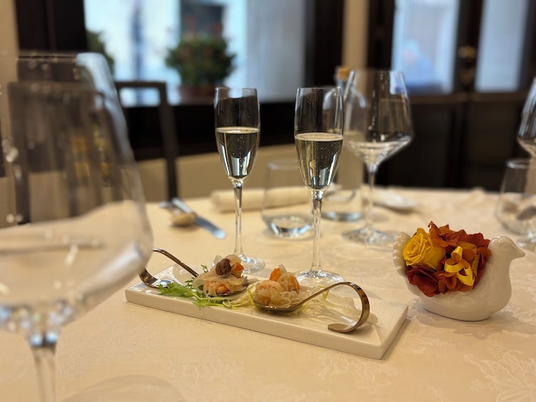A dining table with a white tablecloth, three glasses of water, a plate with seafood appetizers, and a vase with yellow flowers. 3