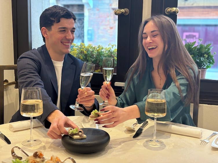 Two people toasting with champagne glasses at a table with a black bowl and a plate of food. 4