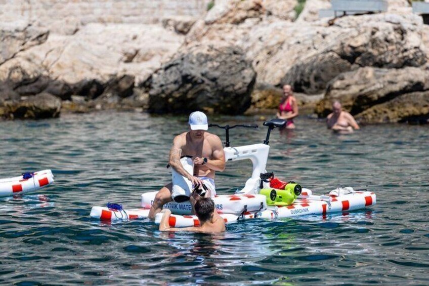 A person on a raft with a sewing machine, surrounded by water and rocks. 5