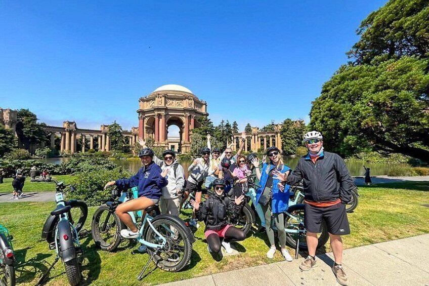 A group of people on bicycles in a park with a large historical building in the background. 2