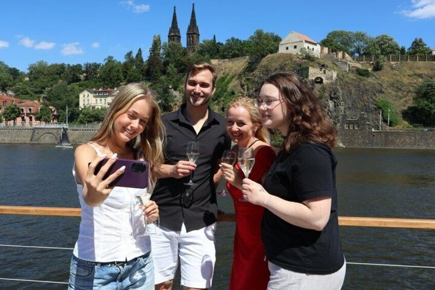 A group of people on a boat with a river and historic buildings in the background. 1