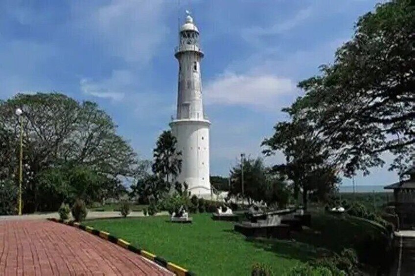 A white lighthouse with a spiral staircase, surrounded by green grass and trees. 1