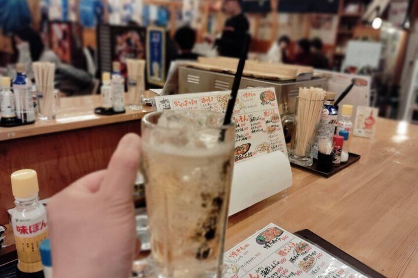 A person holding a glass of iced beverage with a straw, a menu, and condiments on a wooden table in a restaurant. 3