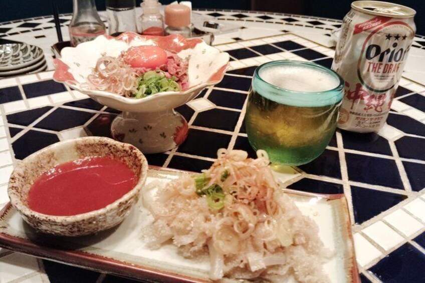 A meal with a bowl of red sauce, a plate of shredded food, and a can of beer on a tiled table. 2