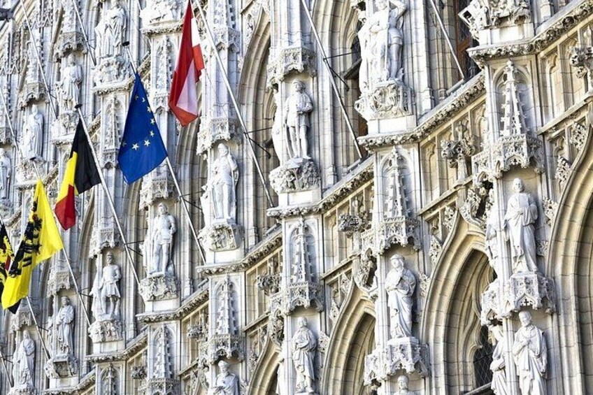 A building facade with intricate stone carvings and multiple flags, including the European Union flag. 1