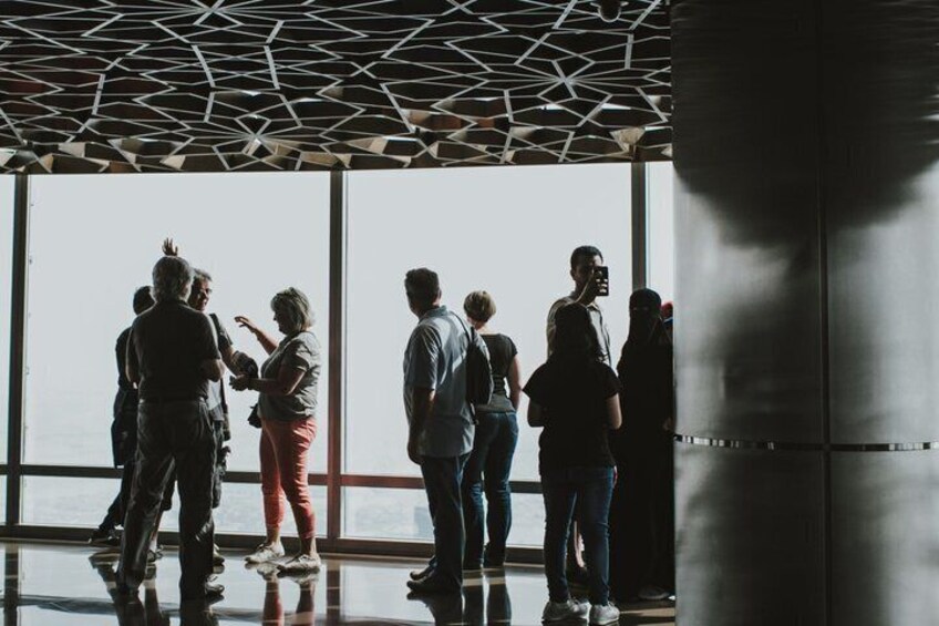 A group of people standing indoors with large windows and a geometric ceiling. 5