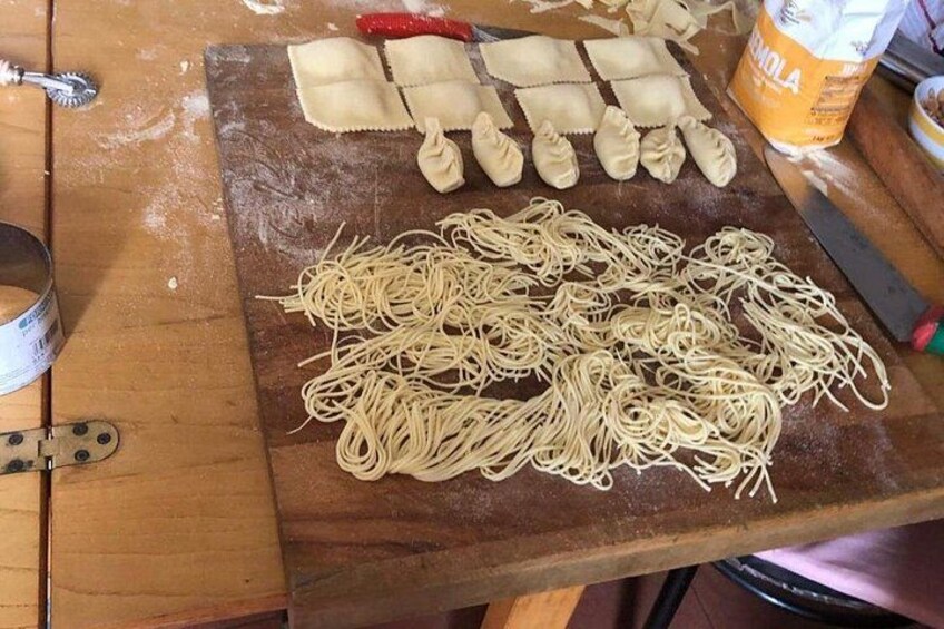 A wooden table with uncooked pasta, a rolling pin, and a container of flour. 5