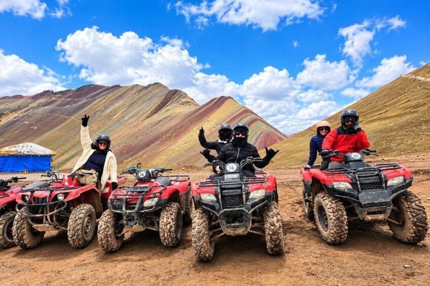 Four people on red ATVs in a desert landscape with mountains in the background. 1