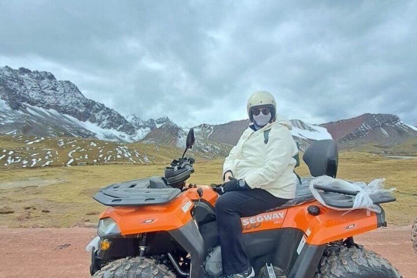 A person on an orange ATV in a mountainous area with snow-capped peaks in the background. 5