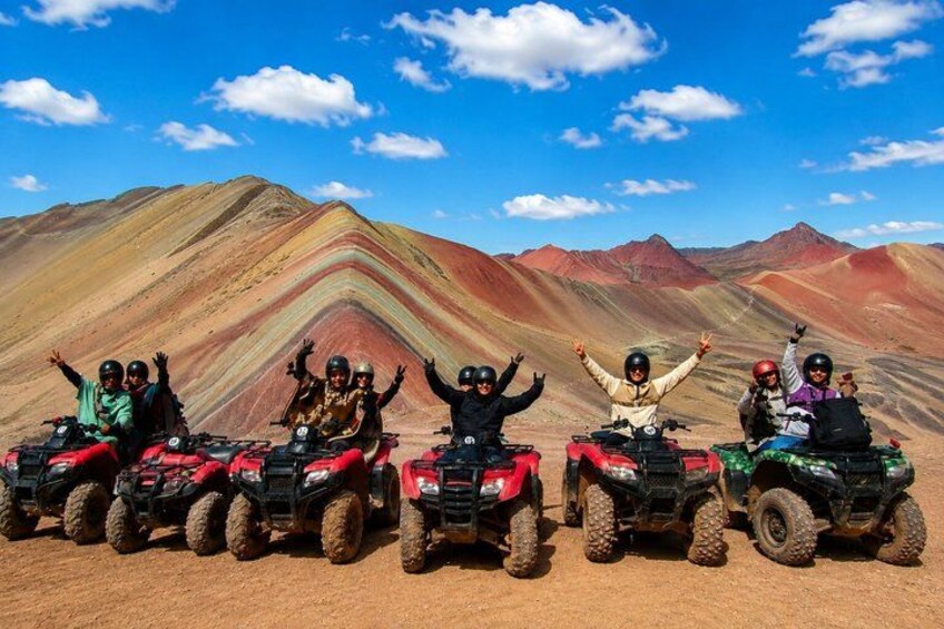 Five people on ATVs in a desert with colorful mountains in the background. 3