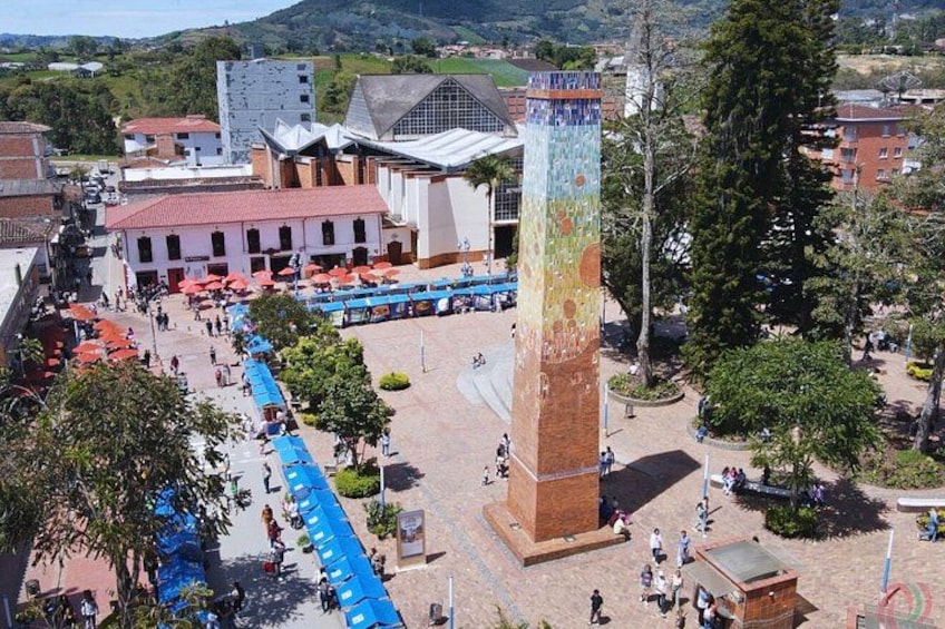 A plaza with a tall tower, a bus station, and buildings with red roofs. 2