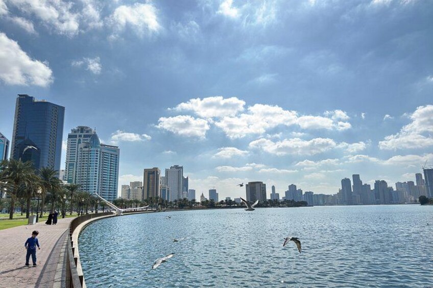 A waterfront with a city skyline, a pedestrian path, and a bird flying over the water. 2