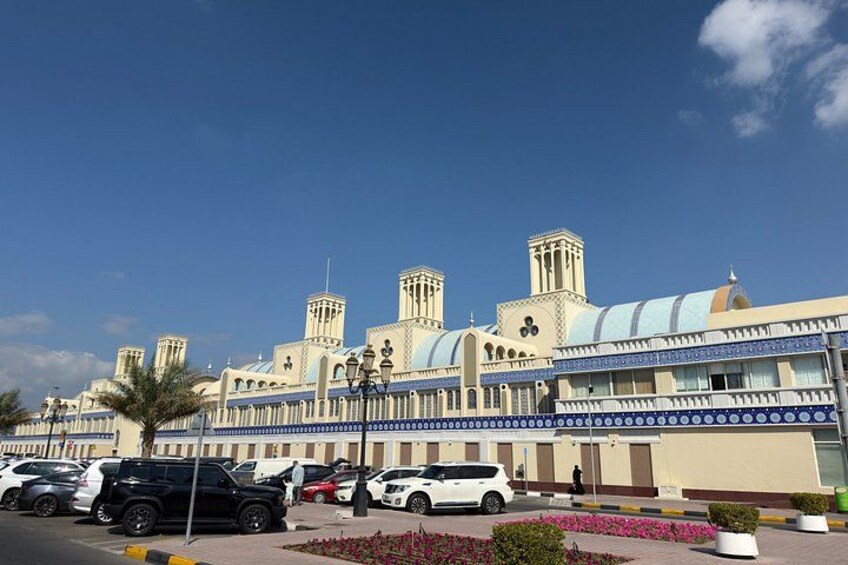 A large building with multiple towers and a blue roof, surrounded by parked cars and a pedestrian walkway. 4