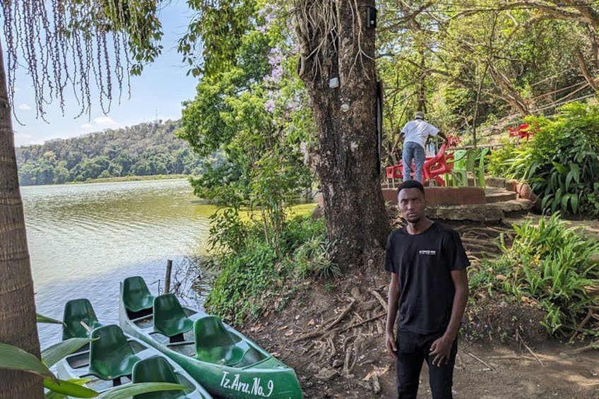 A man standing by a lake with green boats and a tree. 4