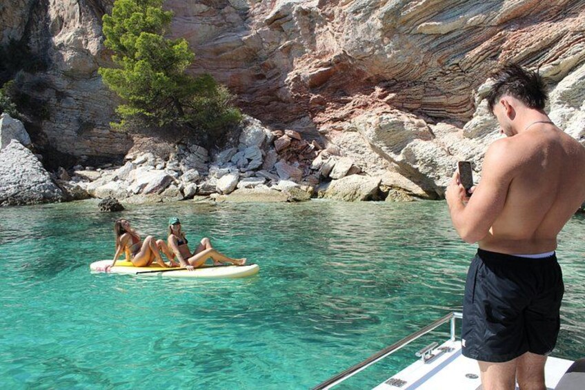 Un hombre fotografiando a dos personas en un bote salvavidas amarillo sobre aguas claras, con acantilados rocosos al fondo. 5