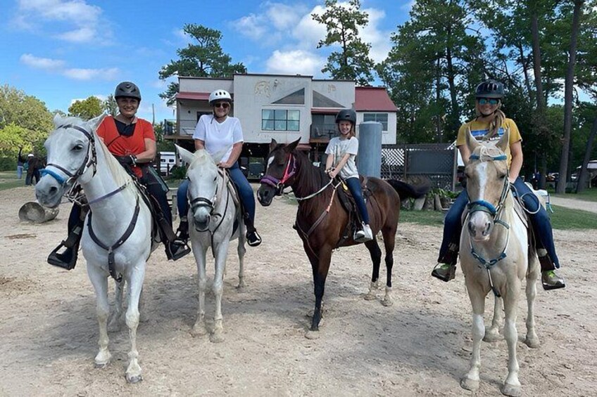 Four people riding horses on a dirt path with a building in the background. 3