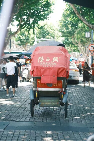 A traditional rickshaw with a red cover parked on a cobblestone street. 3
