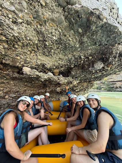 A group of people in a yellow raft, wearing helmets and life vests, surrounded by rocky terrain. 5
