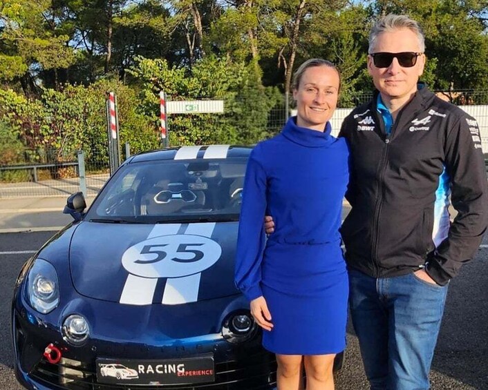 A racing car with the number 55 parked on a road with trees and a fence in the background. 3