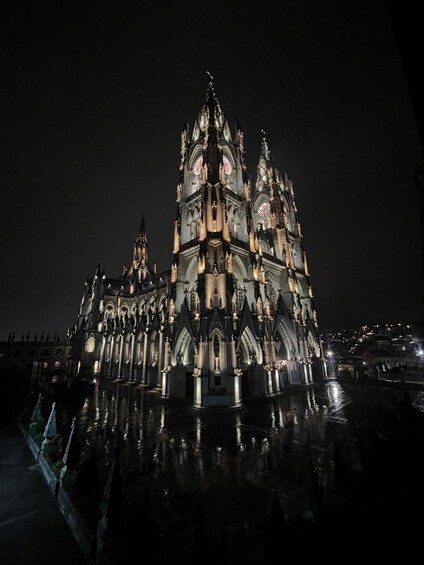 A Gothic-style cathedral with a clock tower, illuminated at night. 3