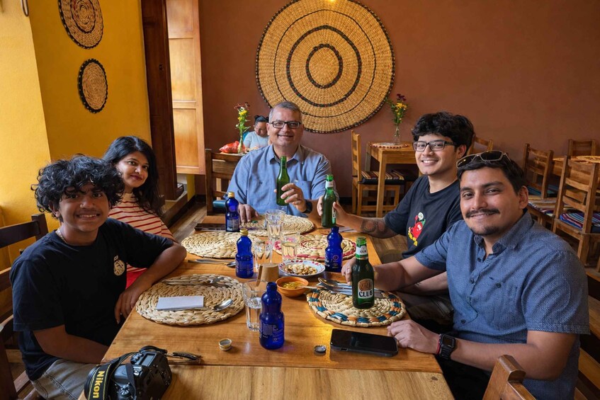A group of people seated around a wooden table with woven placemats, bottles, and a smartphone. 5