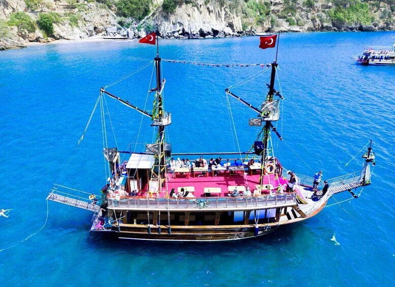 A traditional wooden boat with Turkish flags, anchored in a clear blue sea with rocky cliffs in the background. 1