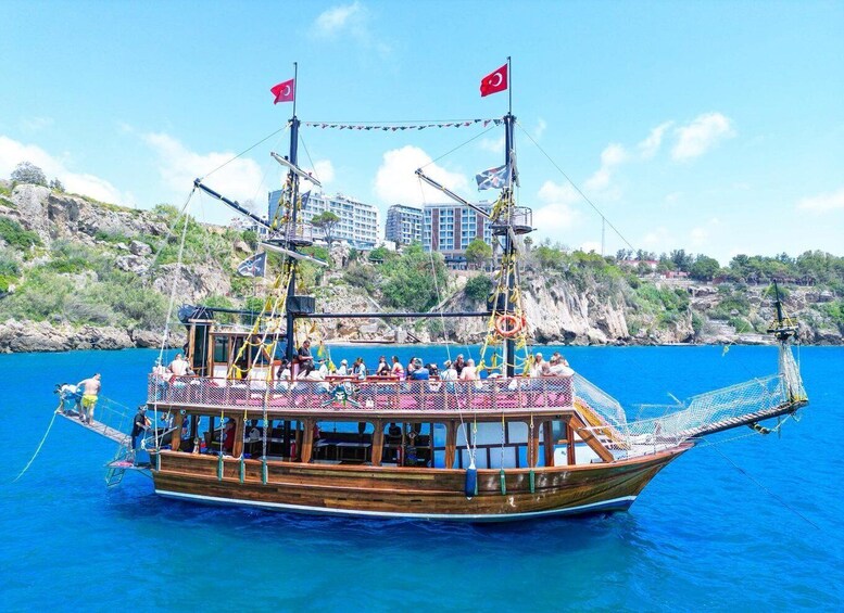 A wooden boat with Turkish flags, passengers, and a rocky coastline in the background. 2