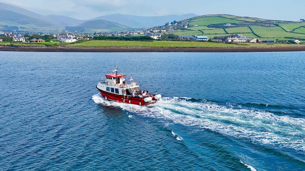 A red and white boat moving through a body of water with a coastal town and green hills in the background. 3