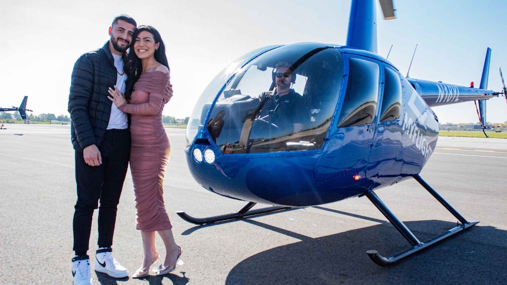 A couple standing next to a blue helicopter on a tarmac. 3