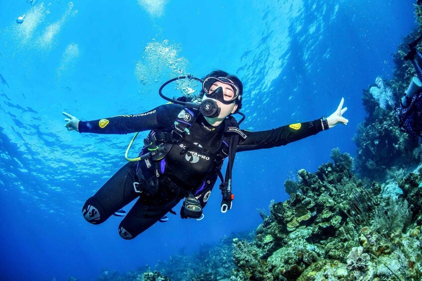 A diver with arms outstretched, surrounded by underwater coral and marine life. 2