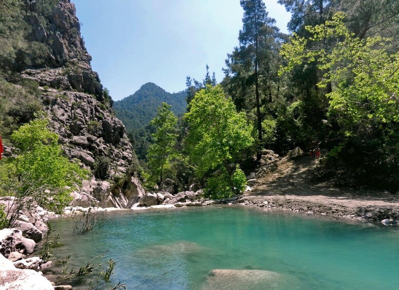 A clear turquoise lake surrounded by rocky cliffs and dense green foliage. 1