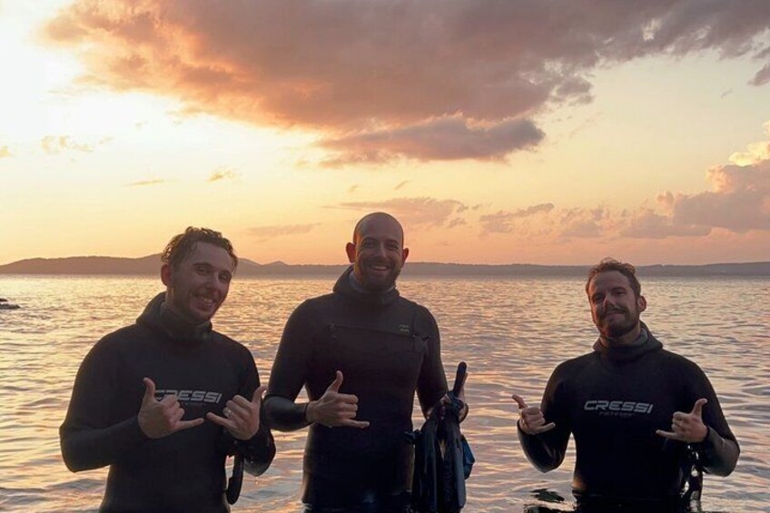 Three people in wetsuits by a body of water during sunset. 5
