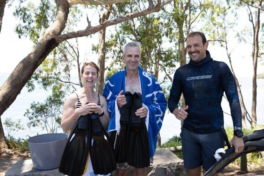 Three people holding diving fins, a bucket, and a tree-lined beach. 2