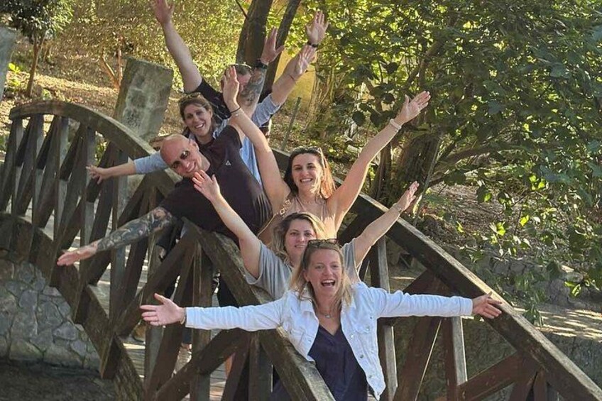 A group of people on a wooden structure with outstretched arms, surrounded by trees and stone walls. 5