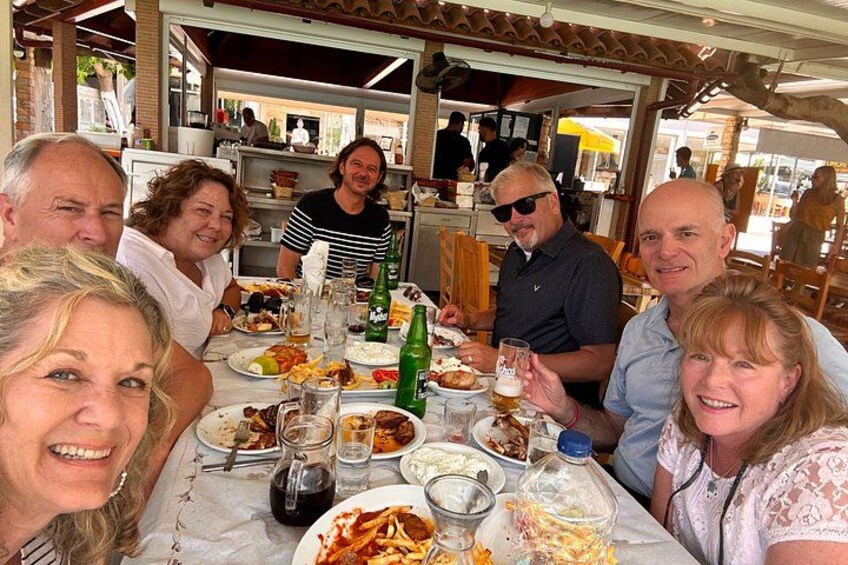 A group of people dining at an outdoor restaurant with various dishes and drinks on the table. 2