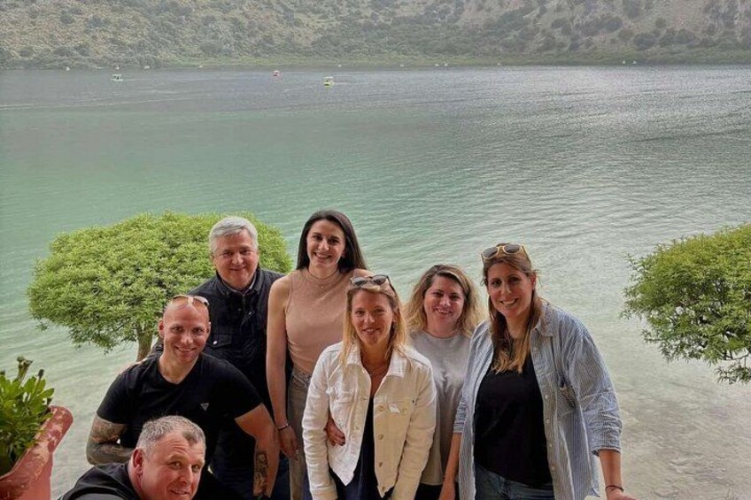 A group of people standing by a lake with a mountainous backdrop. 3
