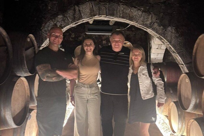 A group of people standing in a cellar with large wooden barrels. 4