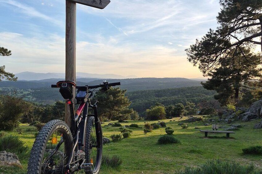 A mountain bike parked on a grassy hill with a wooden signpost in the foreground and a scenic view of a valley in the background. 1