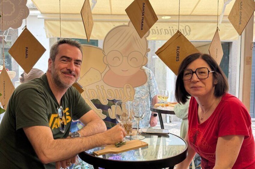 Two people seated at a round table with a glass of wine, surrounded by hanging decorations with text. 4