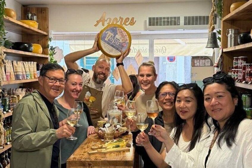A group of people toasting with wine glasses in a store with shelves of products and a sign that reads 'Azores.' 1