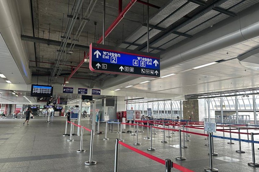 Una terminal de aeropuerto con señales direccionales, una fila de pasajeros y un panel informativo digital. 5