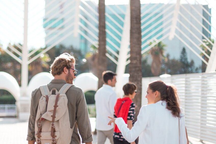 A group of people walking outdoors, palm trees, and modern buildings in the background. 3