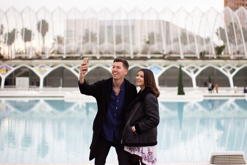 A couple taking a selfie by a pool with a modern architectural structure in the background. 3