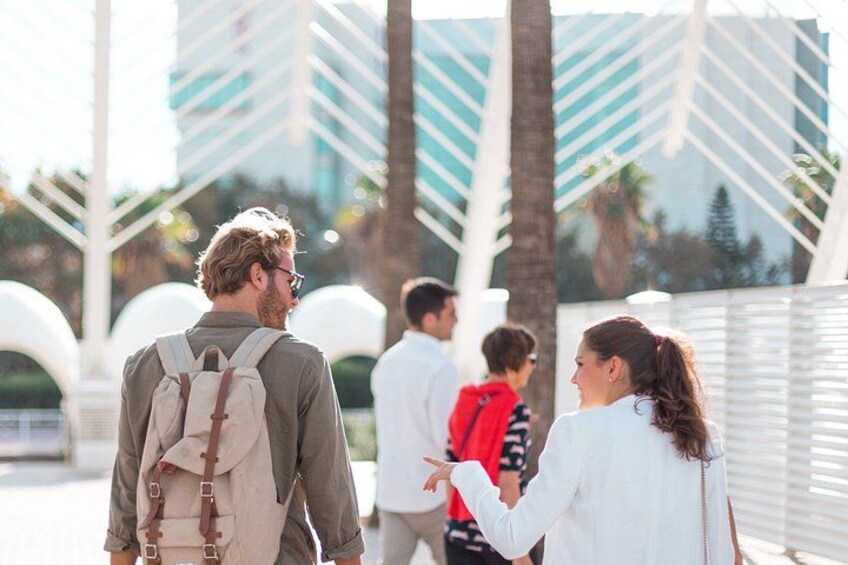 A man with a backpack walking on a bridge, palm trees, and modern buildings in the background. 2