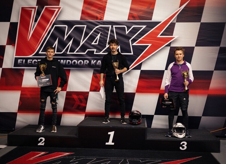 Three individuals on a podium with trophies, standing in front of a checkered background with the text 'VMAX ELECTRONIC KARAOKE'. 2