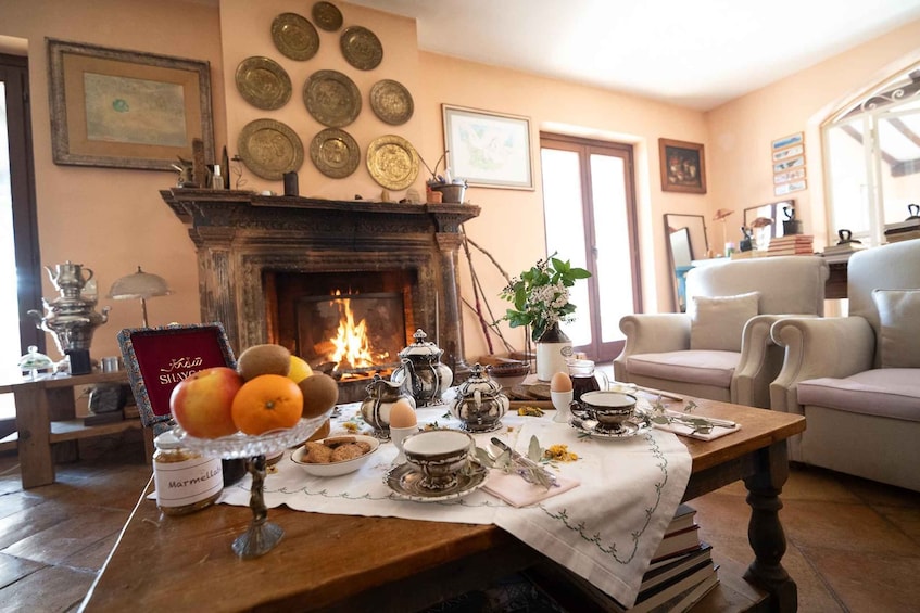 A cozy living room with a fireplace, a table set with tea cups and a fruit bowl, and a sofa in the background. 2